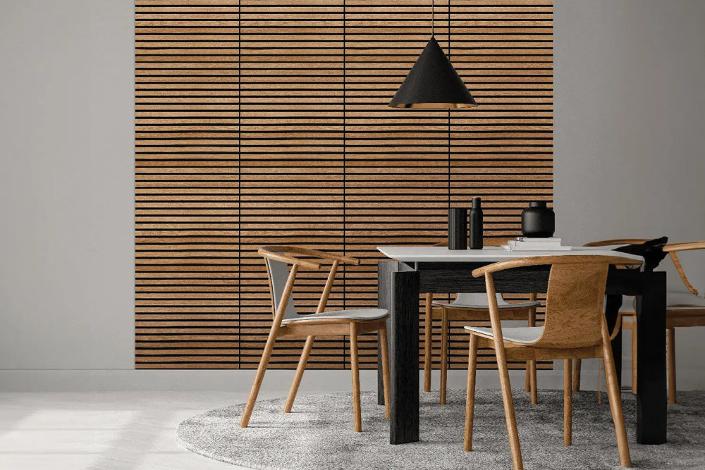 Modern dining room featuring Vantaa Oak acoustic panels as a warm wooden slat wall behind a minimalist white table with black chairs, pendant lamp, and decor.